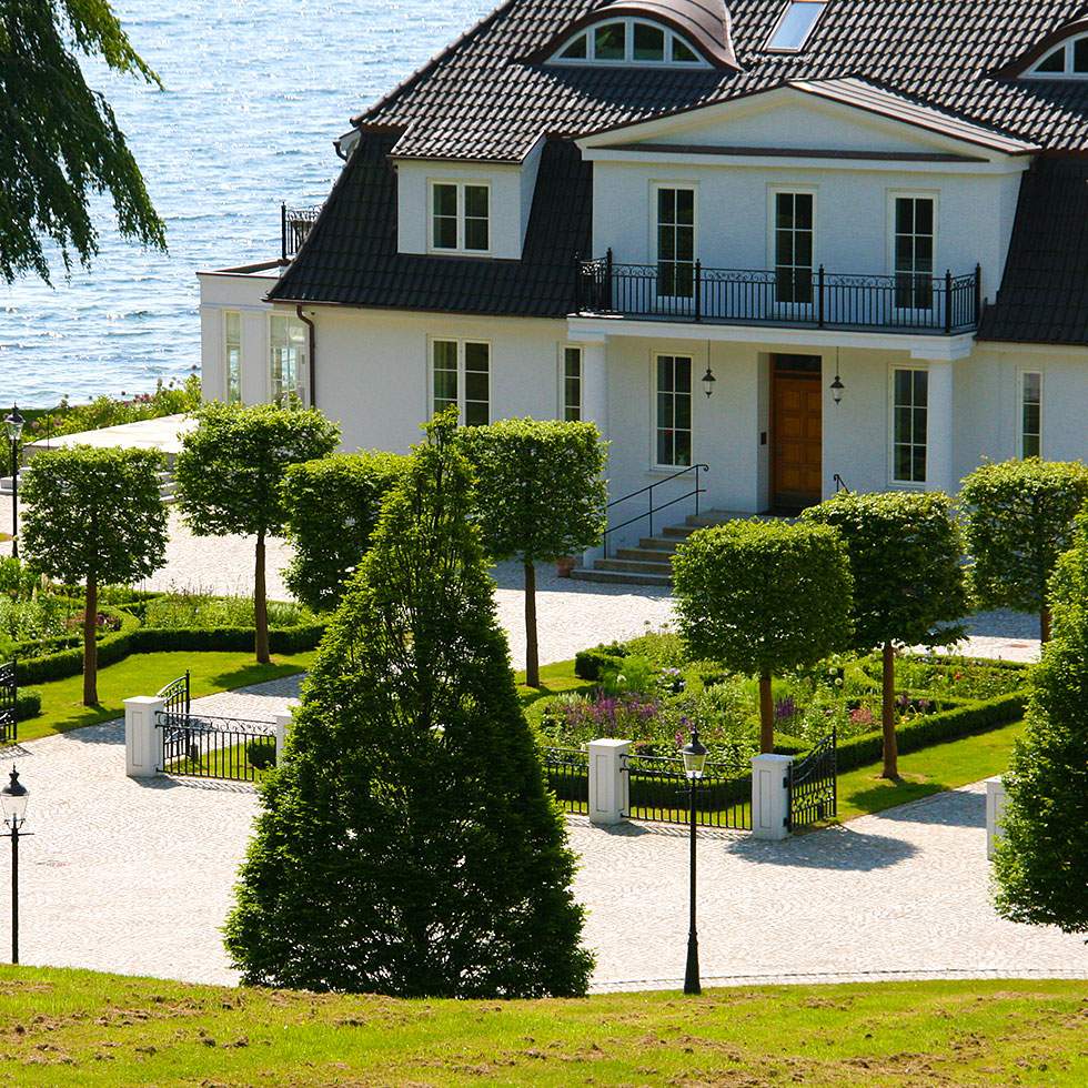 Ein großes weißes Haus mit einem weitläufigen Rasen und hohen Bäumen.