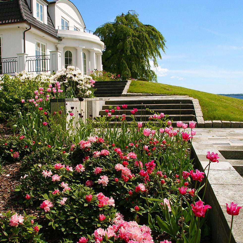 Et rummeligt hus med en stor græsplæne og en farverig blomsterhave.