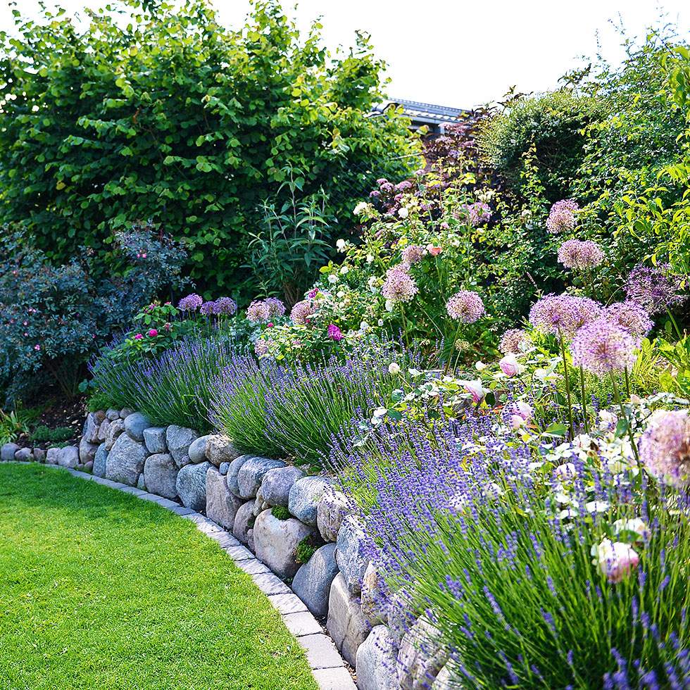 Ein Garten mit Steinmauer und bunten, blühenden Blumen.